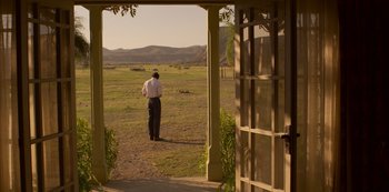 Movie still from “The Crown” (2016), created by Peter Morgan – A man standing in a field looking out of an open door; Extreme Wide shot, Over the shoulder angle