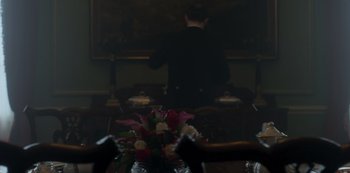 Movie still from “The Crown” (2016), created by Peter Morgan – A man standing in front of a painting in a dark room; Medium shot, Over the shoulder angle