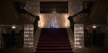 Movie still from “The Crown” (2016), created by Peter Morgan – A woman in a white dress standing at the top of a set of stairs; Wide shot, Low angle