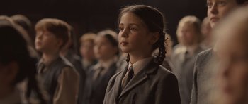 Movie still from “Never Let Me Go” (2010), directed by Mark Romanek – A girl in a suit and tie standing in front of a group of people; Close Up shot, Over the shoulder angle