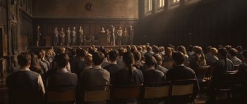 Movie still from “Never Let Me Go” (2010), directed by Mark Romanek – A group of people sitting in front of an audience on a stage; Extreme Wide shot, High angle