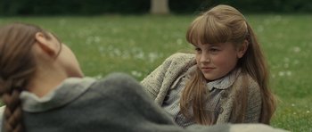 Movie still from “Never Let Me Go” (2010), directed by Mark Romanek – A young girl sitting in the grass looking at the camera; Medium shot, Over the shoulder angle