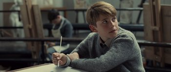 Movie still from “Never Let Me Go” (2010), directed by Mark Romanek – A young boy sitting at a table holding a pencil; Medium shot, Over the shoulder angle