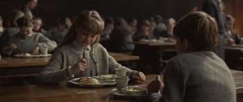 Movie still from “Never Let Me Go” (2010), directed by Mark Romanek – A little girl sitting at a table with a plate of food in front of her; Medium shot, Over the shoulder angle
