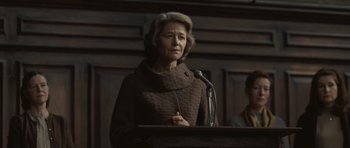Movie still from “Never Let Me Go” (2010), directed by Mark Romanek – An older woman standing at a podium with a microphone; Medium shot, Low angle