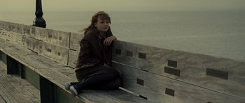 Movie still from “Never Let Me Go” (2010), directed by Mark Romanek – A woman sitting on top of a wooden bench near the ocean; Medium shot, High angle