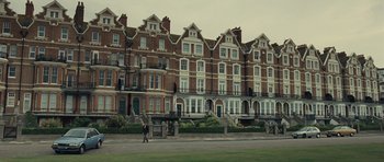 Movie still from “Never Let Me Go” (2010), directed by Mark Romanek – A person walking in front of a row of buildings; Extreme Wide shot, Low angle