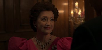 Movie still from “The Crown” (2016), created by Peter Morgan – An older woman in a pink dress and a necklace; Close Up shot, Over the shoulder angle