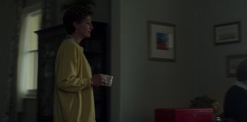 Movie still from “The Crown” (2016), created by Peter Morgan – A woman standing in a living room holding a cup; Medium shot, Low angle
