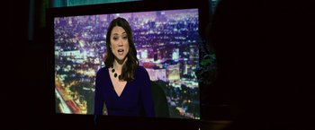 Movie still from “Nightcrawler” (2014), directed by Dan Gilroy – A woman in front of a tv with a city in the background; Medium shot, Over the shoulder angle