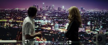 Movie still from “Nightcrawler” (2014), directed by Dan Gilroy – Two people sitting at a table in front of a city skyline; Wide shot, Over the shoulder angle