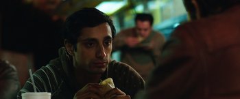 Movie still from “Nightcrawler” (2014), directed by Dan Gilroy – A man eating a hot dog in front of another man; Close Up shot, Over the shoulder angle