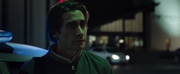 Movie still from “Nightcrawler” (2014), directed by Dan Gilroy – A young man in a green jacket standing next to a car; Close Up shot, Over the shoulder angle