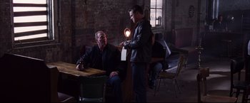 Movie still from “The Departed” (2006), directed by Martin Scorsese – Two men are sitting at a table and one of them is holding a light; Medium shot, Over the shoulder angle