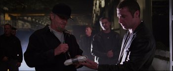 Movie still from “The Departed” (2006), directed by Martin Scorsese – A man is handing something to another man; Medium shot, Over the shoulder angle