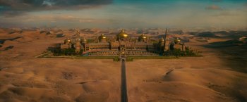 Movie still from “The Dictator” (2012), directed by Larry Charles – An aerial view of a desert with a road leading to it; Extreme Wide shot, High angle