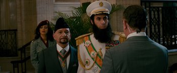 Movie still from “The Dictator” (2012), directed by Larry Charles – A man in a suit with a beard and a hat; Medium shot, Over the shoulder angle