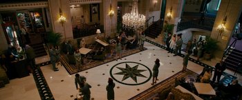 Movie still from “The Dictator” (2012), directed by Larry Charles – A group of people standing in a room with chandeliers; Extreme Wide shot, High angle