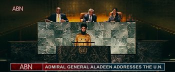 Movie still from “The Dictator” (2012), directed by Larry Charles – A man standing at a podium in front of three other people; Wide shot, Low angle