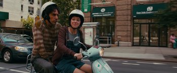 Movie still from “The Dictator” (2012), directed by Larry Charles – A man and a woman riding a scooter down a street; Medium shot, Over the shoulder angle