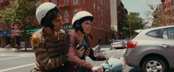 Movie still from “The Dictator” (2012), directed by Larry Charles – A man and a woman riding a scooter down a street; Medium shot, Over the shoulder angle