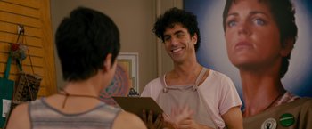 Movie still from “The Dictator” (2012), directed by Larry Charles – A man wearing an apron smiles at a woman; Medium shot, Over the shoulder angle