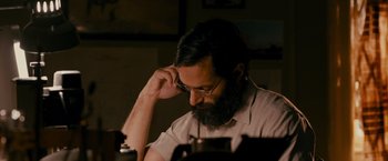 Movie still from “The Dictator” (2012), directed by Larry Charles – A man with a beard is sitting at a table; Close Up shot, High angle
