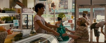Movie still from “The Dictator” (2012), directed by Larry Charles – A woman is handing a bag to a customer; Medium shot, Over the shoulder angle