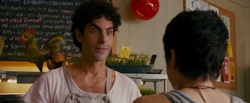 Movie still from “The Dictator” (2012), directed by Larry Charles – A man in an apron is talking to a woman in an apron; Close Up shot, Over the shoulder angle