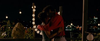 Movie still from “The Dictator” (2012), directed by Larry Charles – A man and a woman embracing in front of a string light; Medium shot, Overhead angle