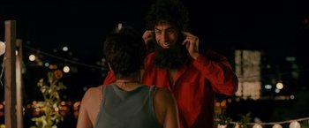 Movie still from “The Dictator” (2012), directed by Larry Charles – A man in a red shirt is putting on a fake beard; Close Up shot, Over the shoulder angle