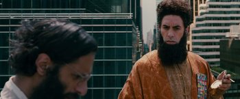 Movie still from “The Dictator” (2012), directed by Larry Charles – A man with long hair and a beard standing next to a woman; Close Up shot, Over the shoulder angle