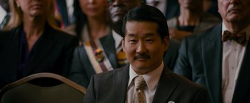 Movie still from “The Dictator” (2012), directed by Larry Charles – A person wearing a suit and tie; Close Up shot, Over the shoulder angle
