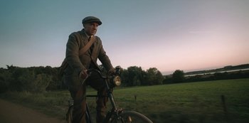 Movie still from “The Dig” (2021), directed by Simon Stone – A man riding a bicycle in a field; Medium shot, Low angle