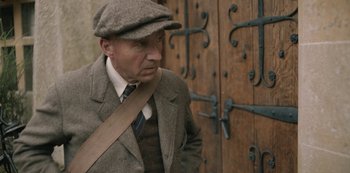 Movie still from “The Dig” (2021), directed by Simon Stone – An older man wearing a hat and a jacket; Medium shot, Over the shoulder angle