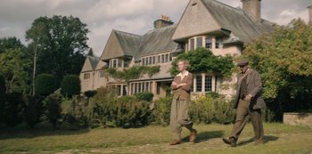 Movie still from “The Dig” (2021), directed by Simon Stone – An older woman standing in front of a large house; Wide shot, Low angle
