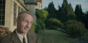 Movie still from “The Dig” (2021), directed by Simon Stone – A person wearing a suit and tie; Medium shot, Over the shoulder angle