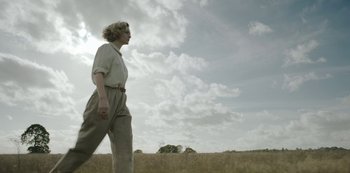 Movie still from “The Dig” (2021), directed by Simon Stone – A woman walking through a field of grass; Wide shot, Low angle