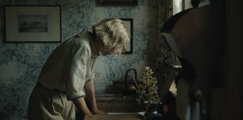 Movie still from “The Dig” (2021), directed by Simon Stone – A woman standing in front of a wooden table; Medium shot, High angle