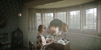 Movie still from “The Dig” (2021), directed by Simon Stone – A woman sitting in front of a mirror in front of a vanity; Medium shot, High angle