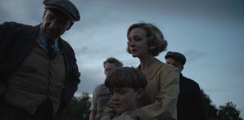 Movie still from “The Dig” (2021), directed by Simon Stone – An older woman and a young boy are standing in a crowd; Medium shot, Low angle