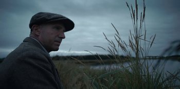 Movie still from “The Dig” (2021), directed by Simon Stone – A man wearing a hat standing next to tall grass; Close Up shot, Low angle