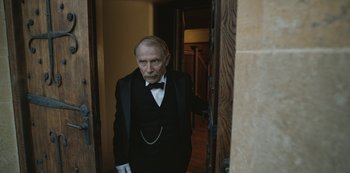 Movie still from “The Dig” (2021), directed by Simon Stone – An old man in a tuxedo standing in front of a door; Medium shot, Low angle
