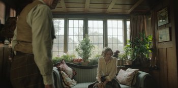 Movie still from “The Dig” (2021), directed by Simon Stone – A woman sitting on top of a couch next to a man; Wide shot, Over the shoulder angle