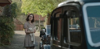 Movie still from “The Dig” (2021), directed by Simon Stone – A woman holding a baby standing in front of an old car; Medium shot, Over the shoulder angle
