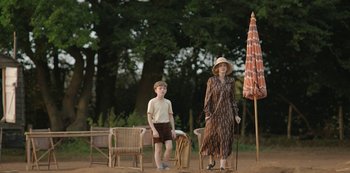 Movie still from “The Dig” (2021), directed by Simon Stone – A woman and a boy standing next to each other in front of chairs; Wide shot, Over the shoulder angle