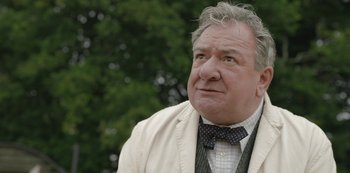 Movie still from “The Dig” (2021), directed by Simon Stone – An older man wearing a suit and bow tie; Close Up shot, Low angle
