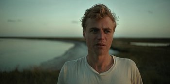 Movie still from “The Dig” (2021), directed by Simon Stone – A man with blonde hair is standing in front of a body of water; Close Up shot, Low angle