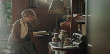 Movie still from “The Dig” (2021), directed by Simon Stone – A woman sitting at a desk with a book in front of her face; Medium shot, High angle
