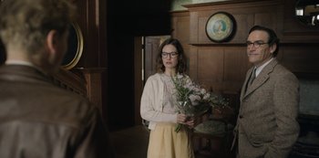 Movie still from “The Dig” (2021), directed by Simon Stone – A woman holding a bouquet of flowers in a room; Medium shot, Over the shoulder angle
